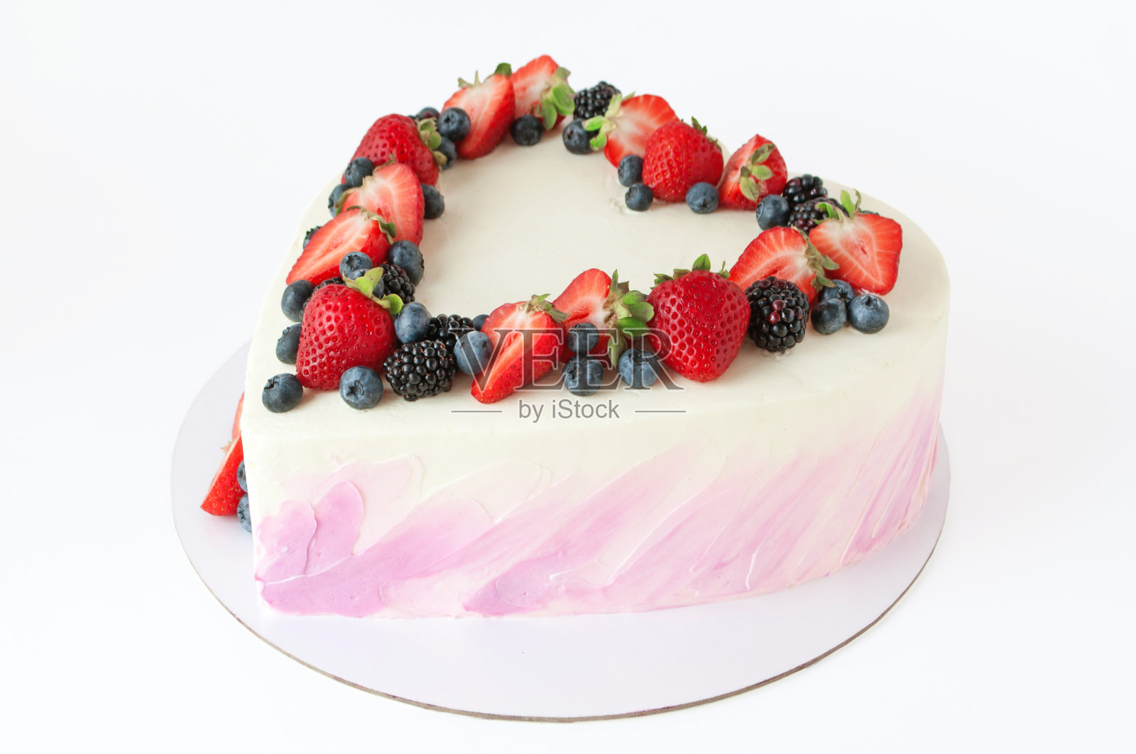 情人节心形蛋糕，上面有粉红色的奶油，以草莓、蓝莓和黑莓装饰，白色的背景。照片摄影图片