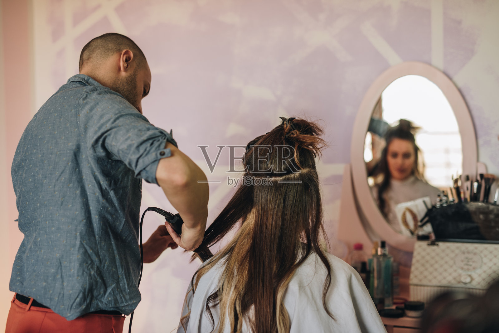 男发型师在沙龙里给女人拉直头发。照片摄影图片