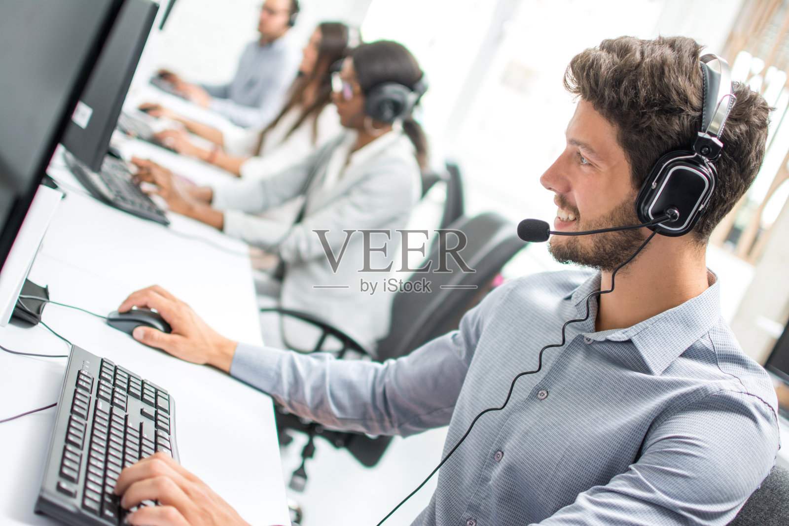 微笑英俊的男性客户支持电话接线员与耳机工作在呼叫中心。照片摄影图片