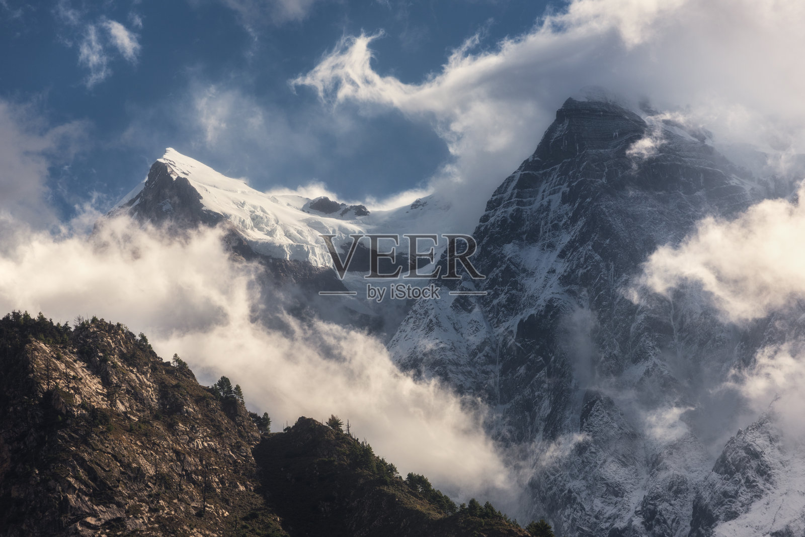 壮丽的风景与雪峰在尼泊尔云中。日落时，美丽的高高的岩石和戏剧性的多云天空构成了多彩的风景。自然背景。童话场景。神奇的山照片摄影图片