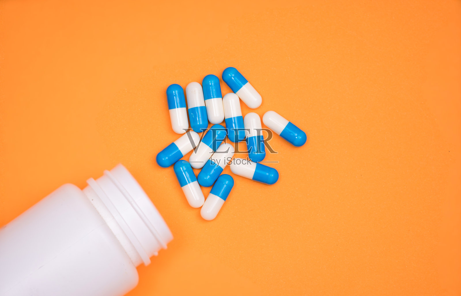 抗生素药用胶囊从瓶中掉落，背景为橙色照片摄影图片