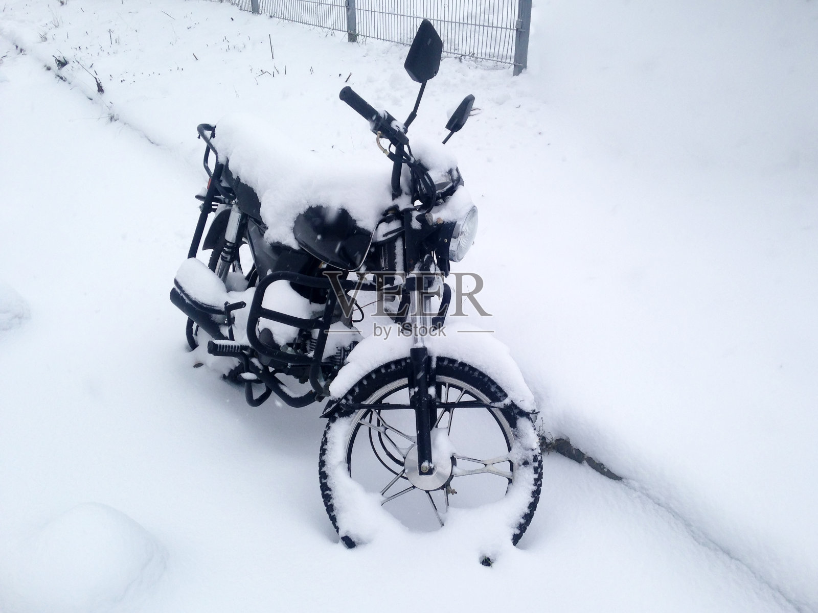 摩托车被雪覆盖在城市的停车场里。照片摄影图片