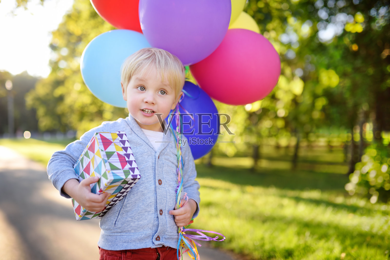 可爱的男孩拿着一束彩色气球和礼物在一个节日盒。生日快乐!照片摄影图片