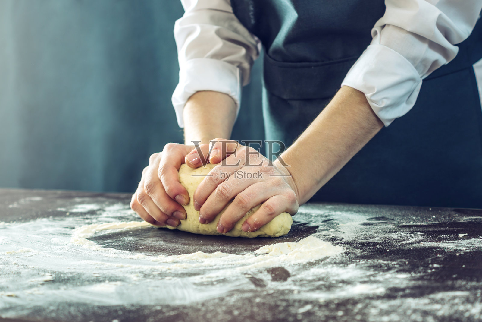 穿着黑围裙的厨师用你的手在桌子上做披萨面团照片摄影图片