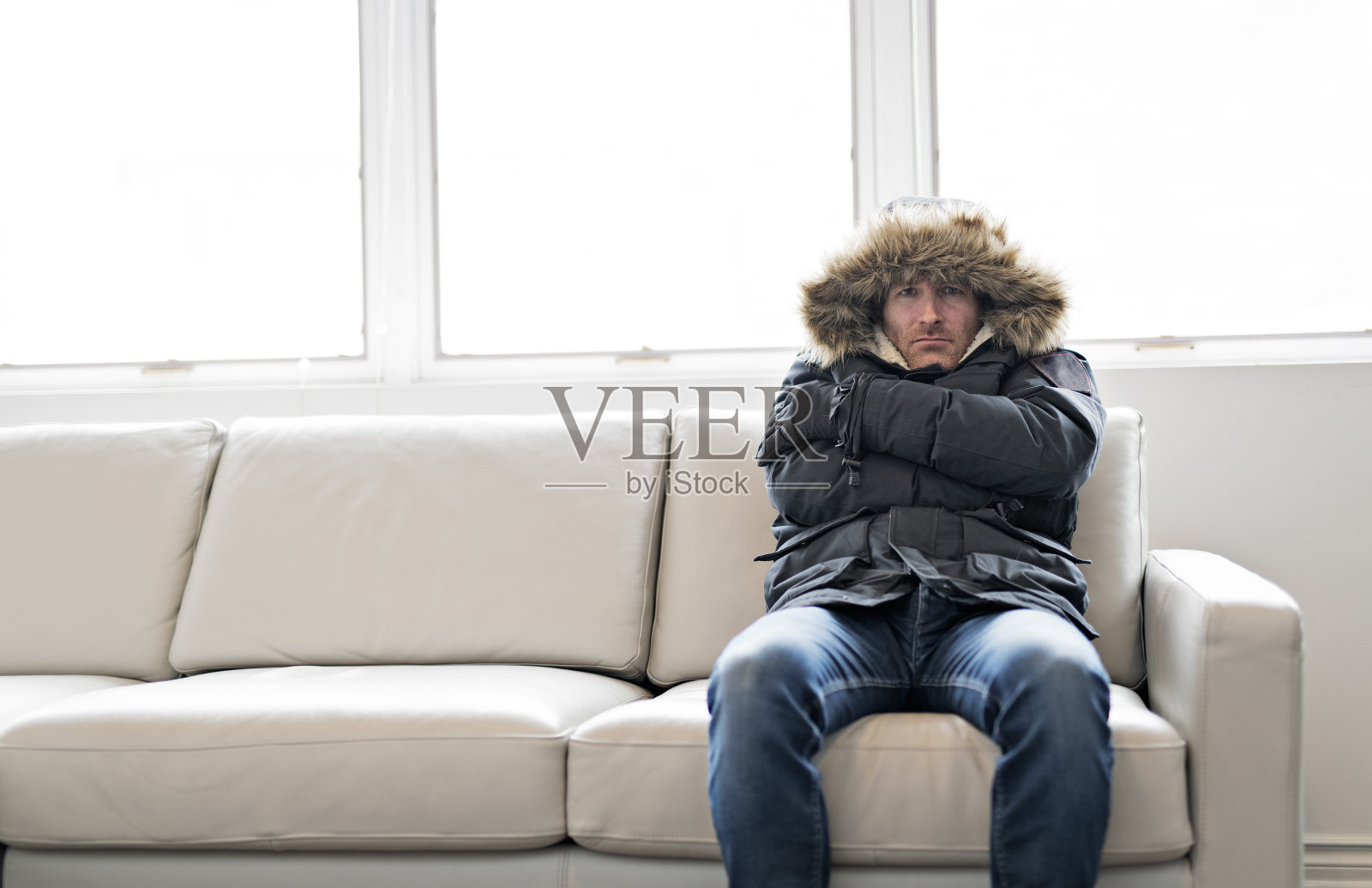 穿着暖和衣服，坐在沙发上感受屋内寒冷的男人照片摄影图片