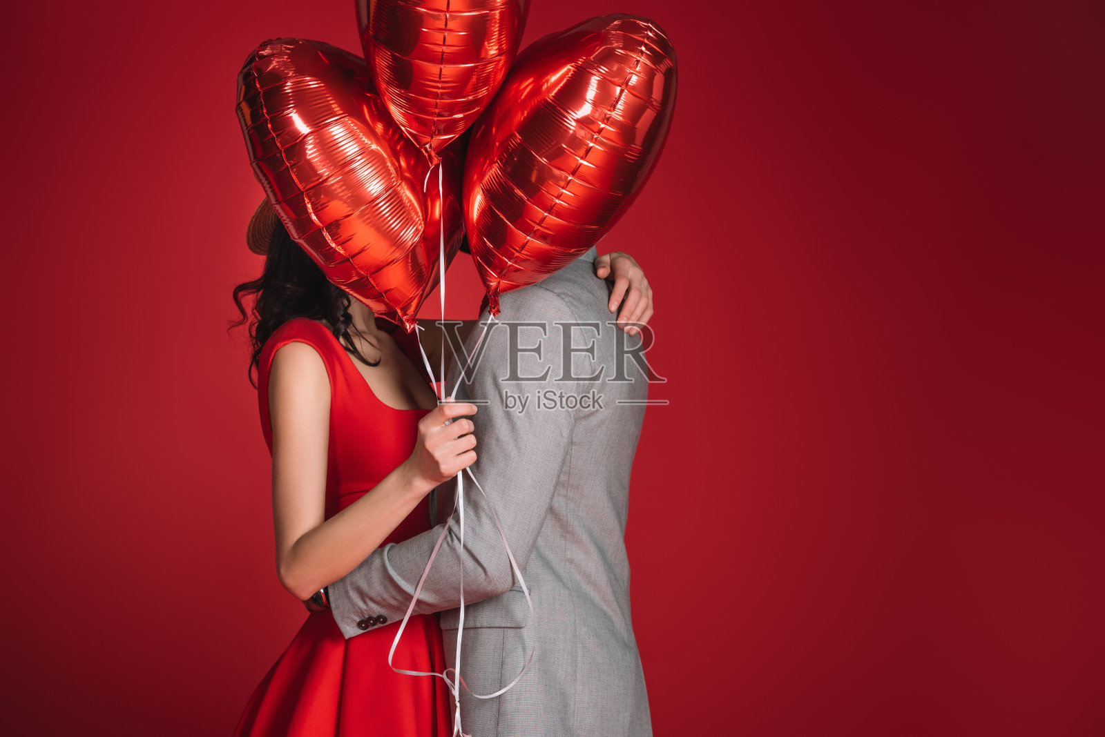 一对夫妇用一捆孤立在红色上的气球遮住脸照片摄影图片