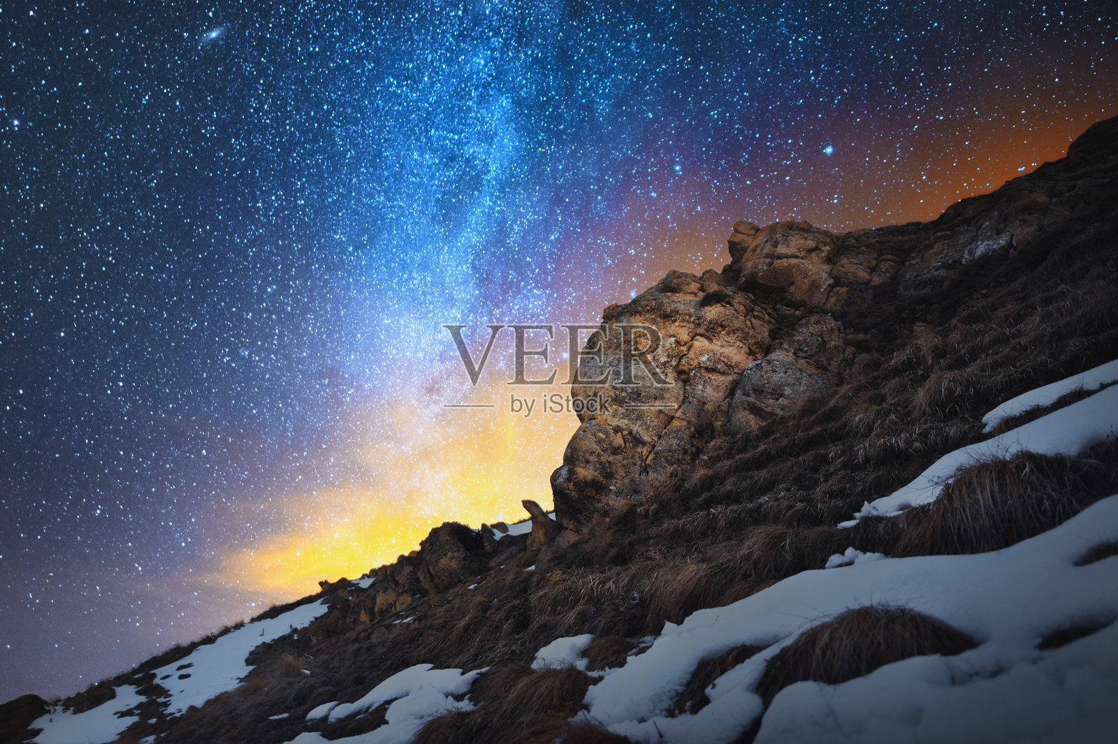 长曝光的夜景。这是一幅美丽的白种人风景画，红色的岩石映衬着寒冷的银河系，岩石后面的地平线上散发着温暖的淡黄色光芒照片摄影图片