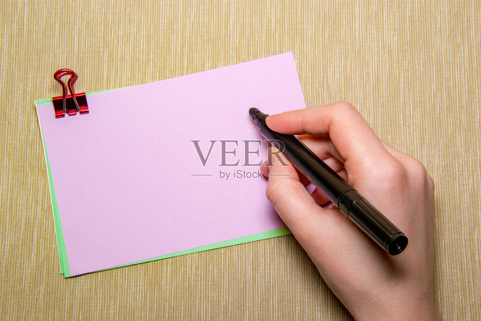 粉红色的纸上有回形针，一个女人手里拿着笔准备写字。黄色隔离的对象照片摄影图片