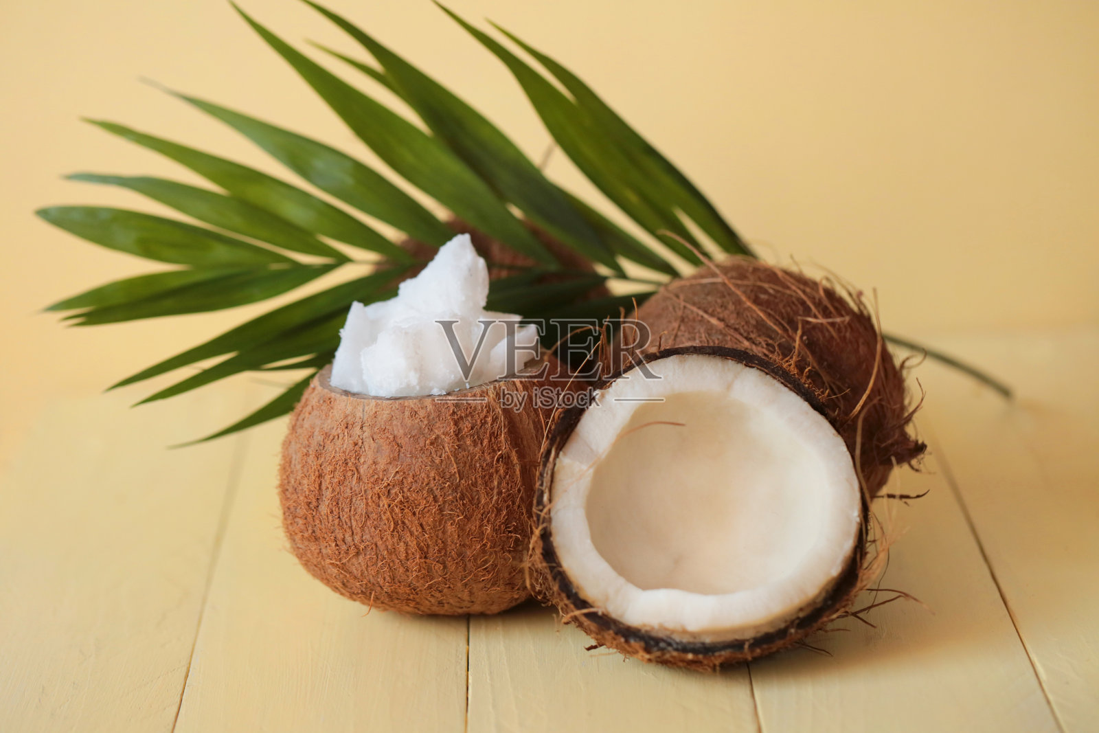 天然椰子油。椰子在一块切开，椰子油片在椰子壳上，棕榈叶在黄色木板上作背景照片摄影图片