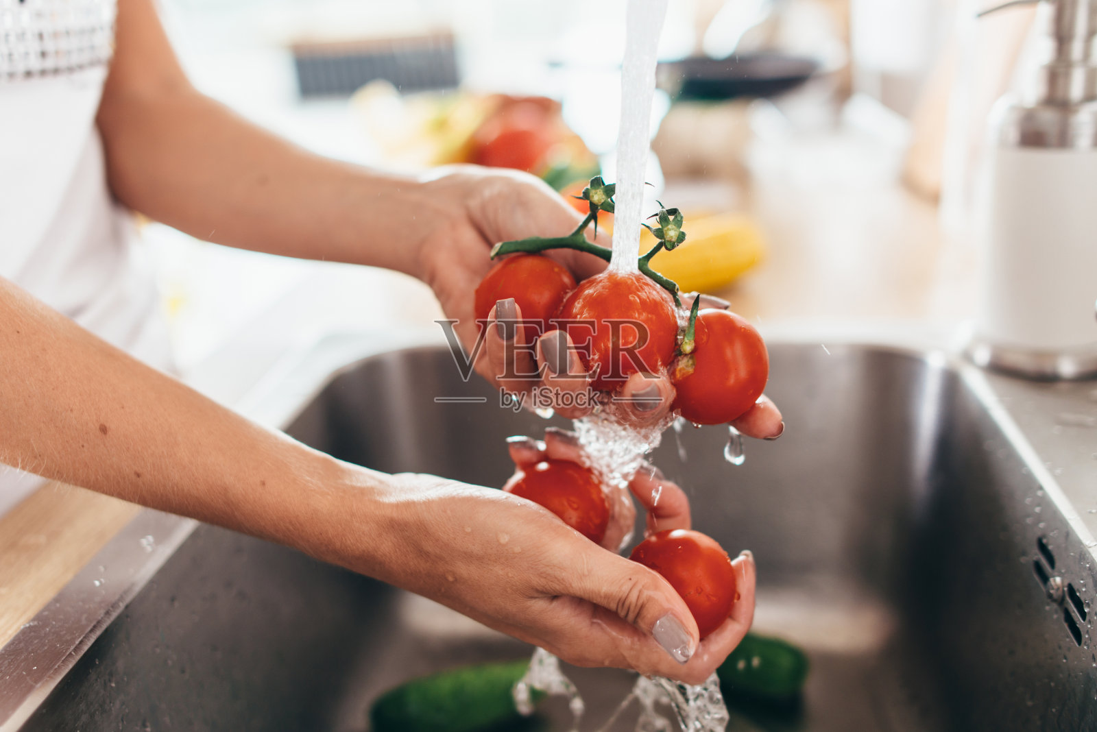 在厨房水槽里洗西红柿的女人。照片摄影图片