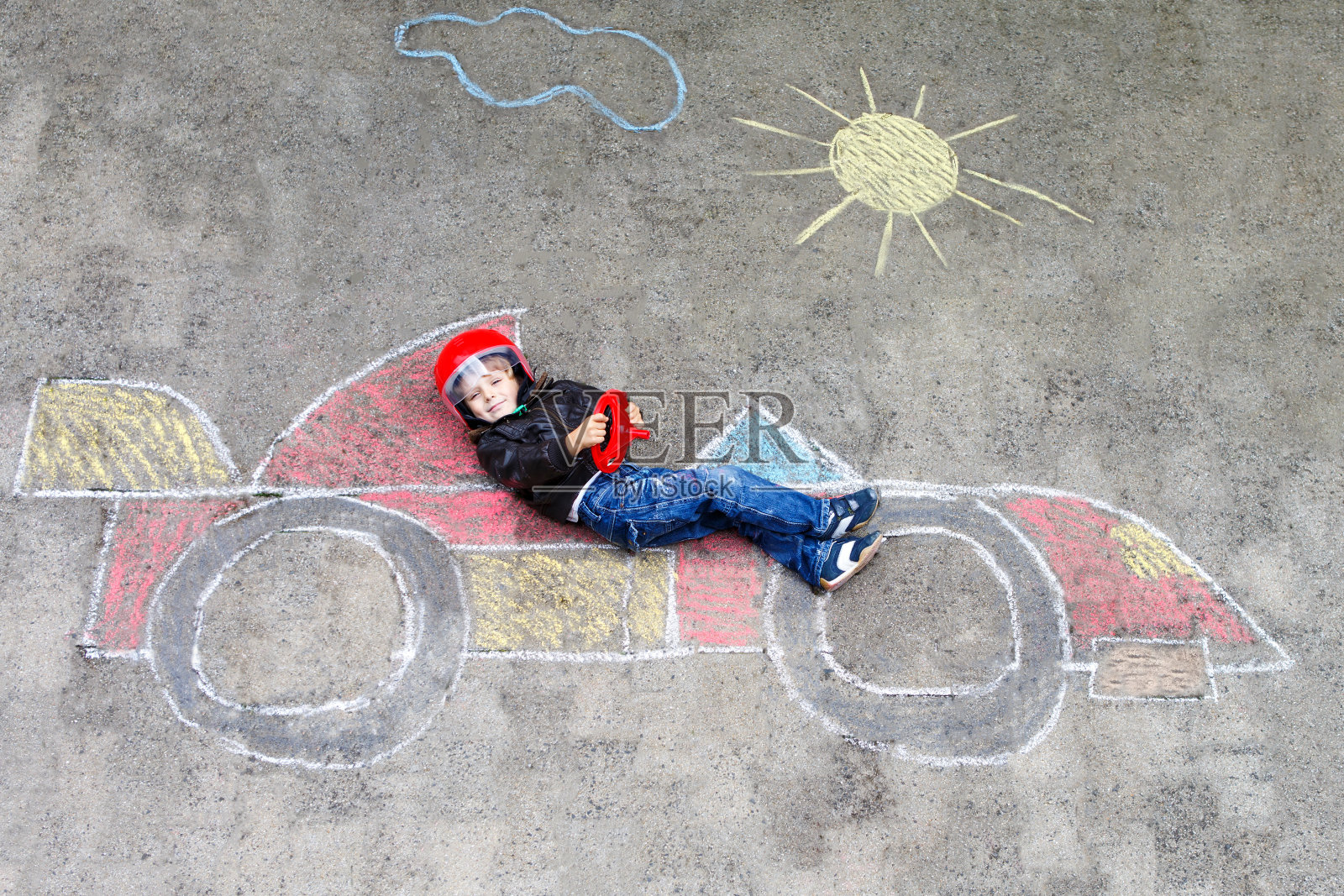 可爱的小男孩用彩色粉笔在沥青上画赛车画。照片摄影图片