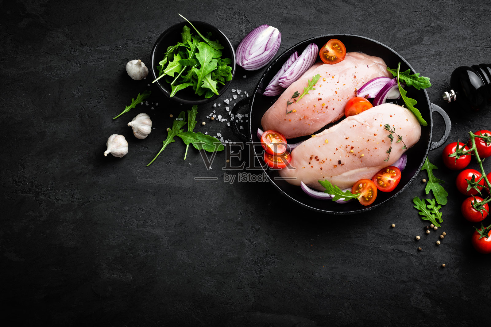 新鲜的生鸡肉，用香料腌制的鱼片，洋葱和西红柿在黑色的背景。俯视图照片摄影图片