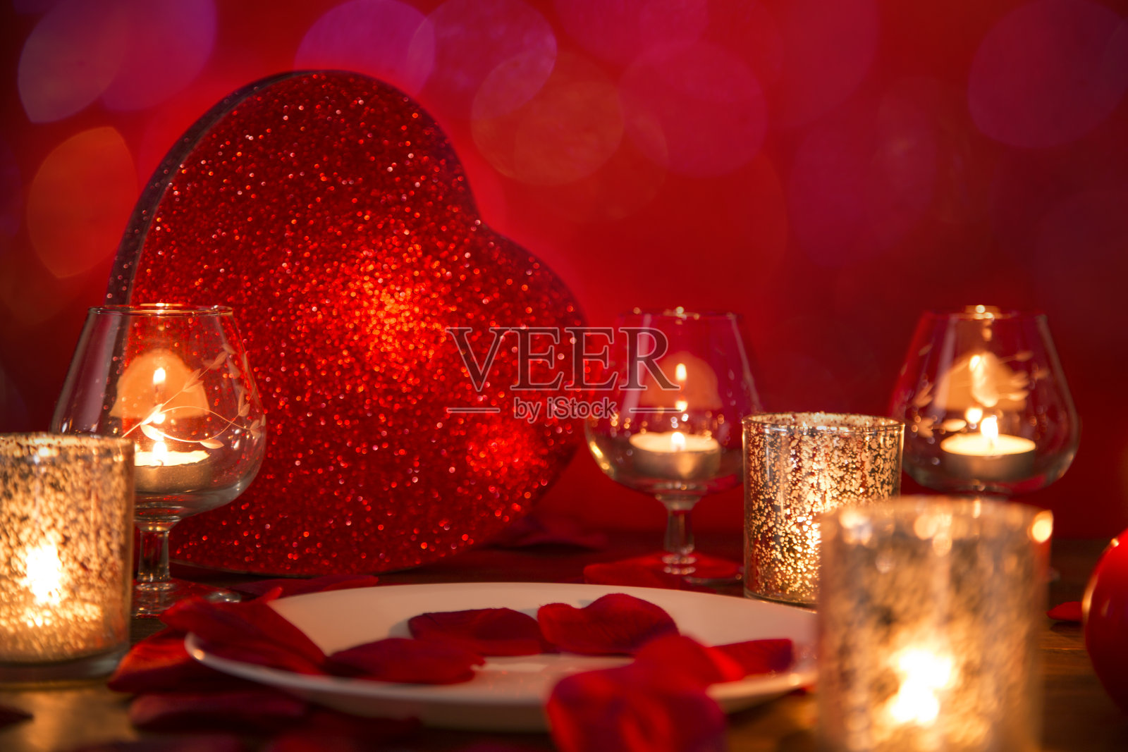 情人节的浪漫烛光晚餐与心和玫瑰花瓣。照片摄影图片