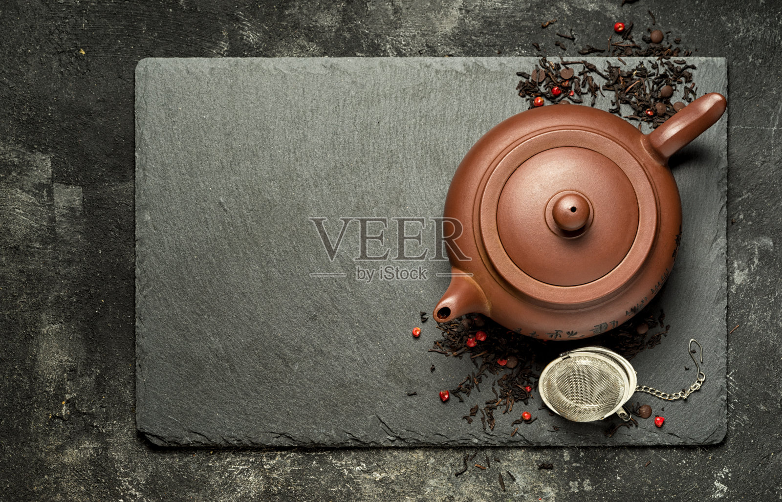 传统的棕色粘土茶壶放在一个黑色的石头托盘，中国红茶和干浆果和小巧克力。顶部视图与复制空间。照片摄影图片