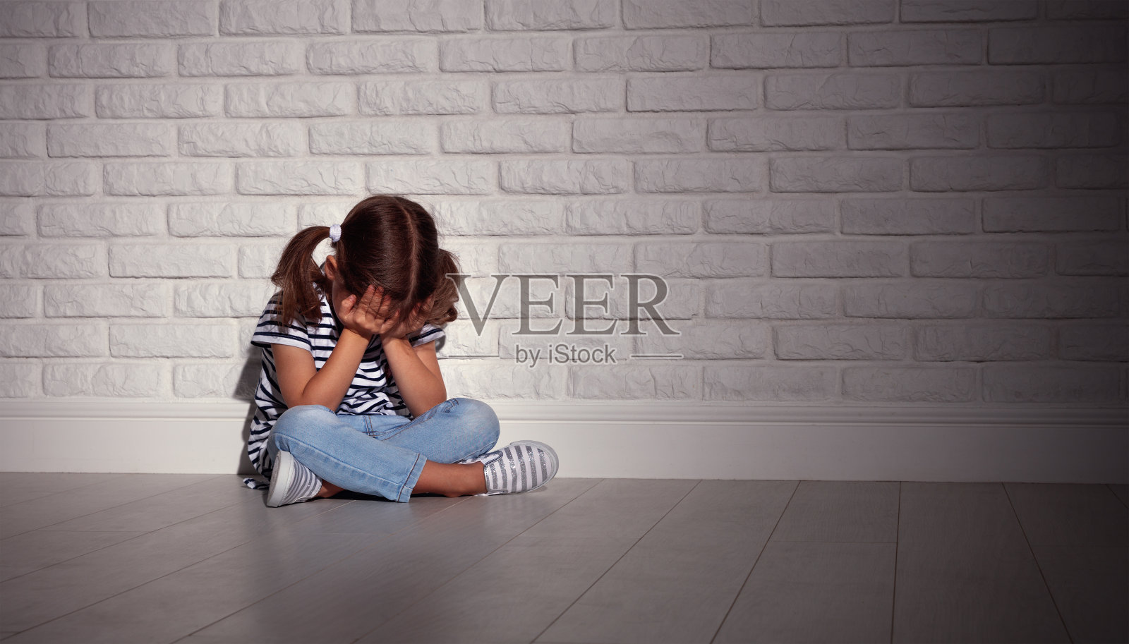 伤心悲伤的小女孩在压力下在一堵黑暗的空墙前哭泣照片摄影图片