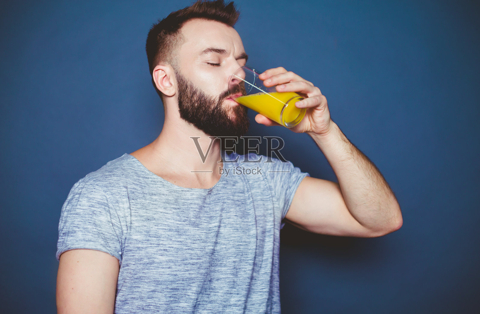 身穿t恤的帅气年轻人，灰色背景上放着一杯鲜橙汁。健康的生活方式。照片摄影图片