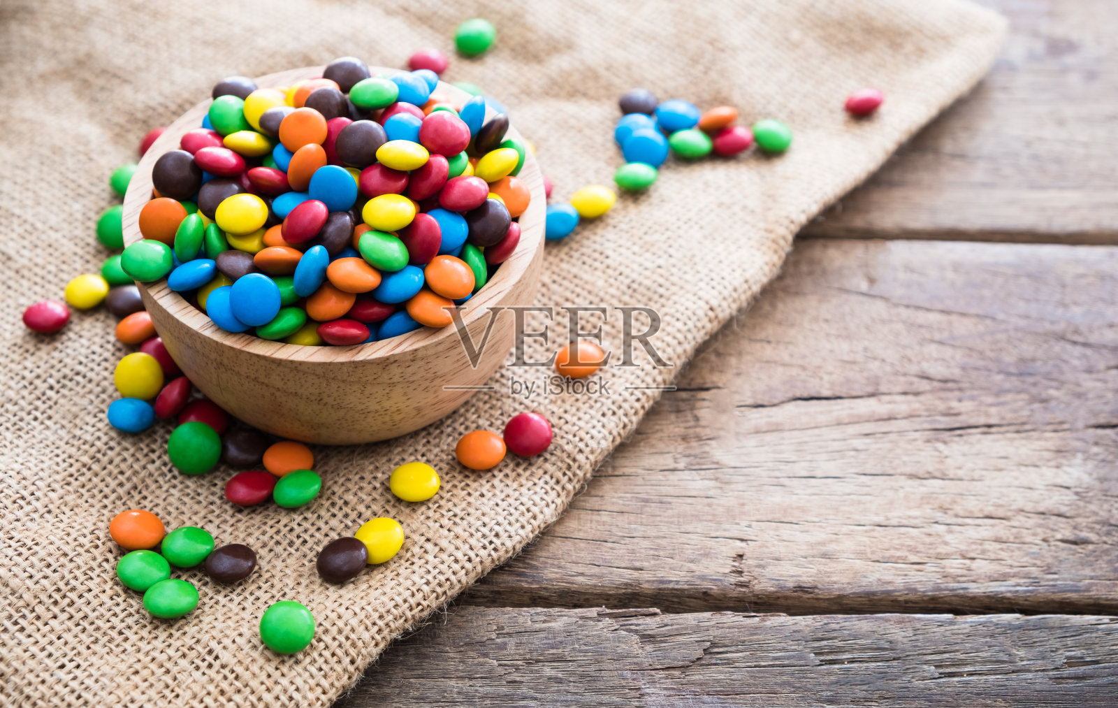 五颜六色的圆巧克力糖果放在木碗里，麻袋布放在木桌上照片摄影图片