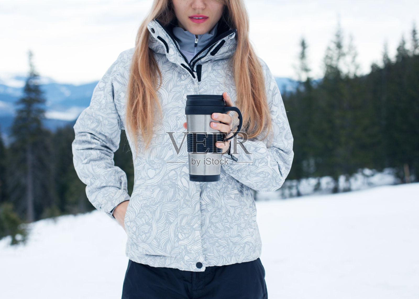 女孩拿着一杯咖啡，背景是冬季的群山照片摄影图片