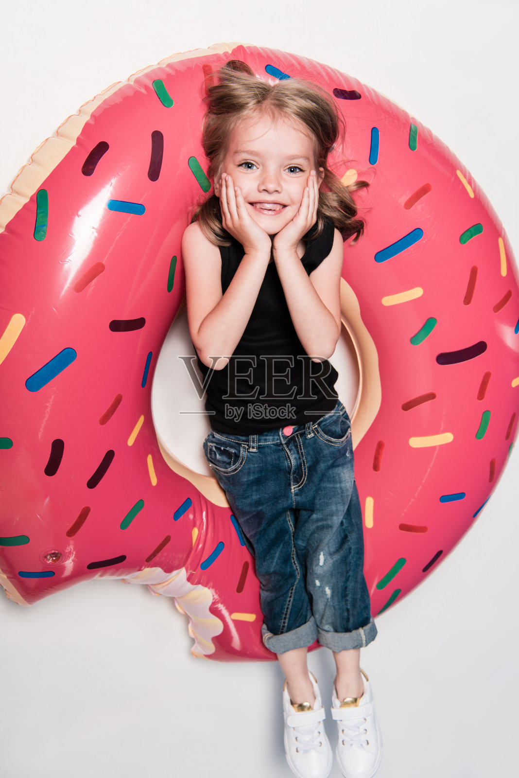 小女孩微笑着躺在以甜甜圈形状的游泳管上照片摄影图片