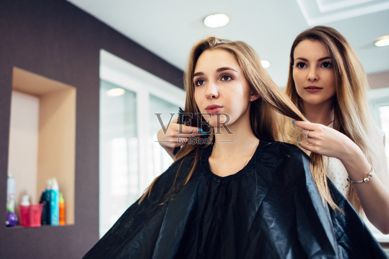 发型师和年轻的女顾客一起在美发厅里决定剪什么发型。两个漂亮的金发女郎在讨论新发型。照片摄影图片