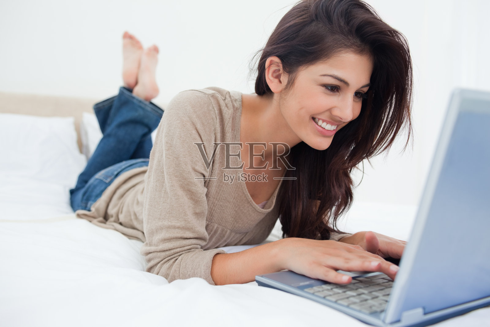 一个女人躺在床上，她的笔记本电脑在她面前，微笑着照片摄影图片