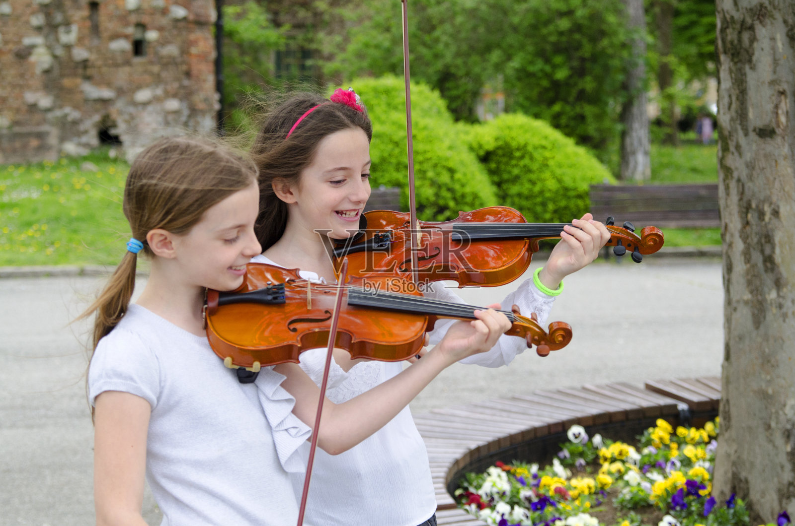 两个小女孩在公园拉小提琴。春天美好的一天照片摄影图片