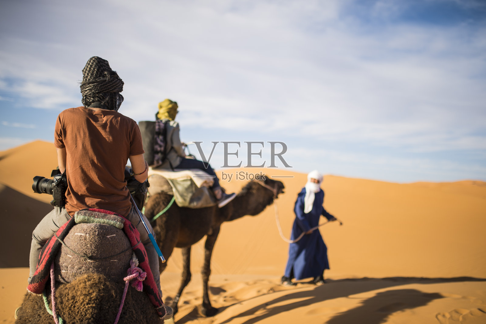 日落时分，游客骑着骆驼穿过撒哈拉沙漠的沙丘——摩洛哥。照片摄影图片