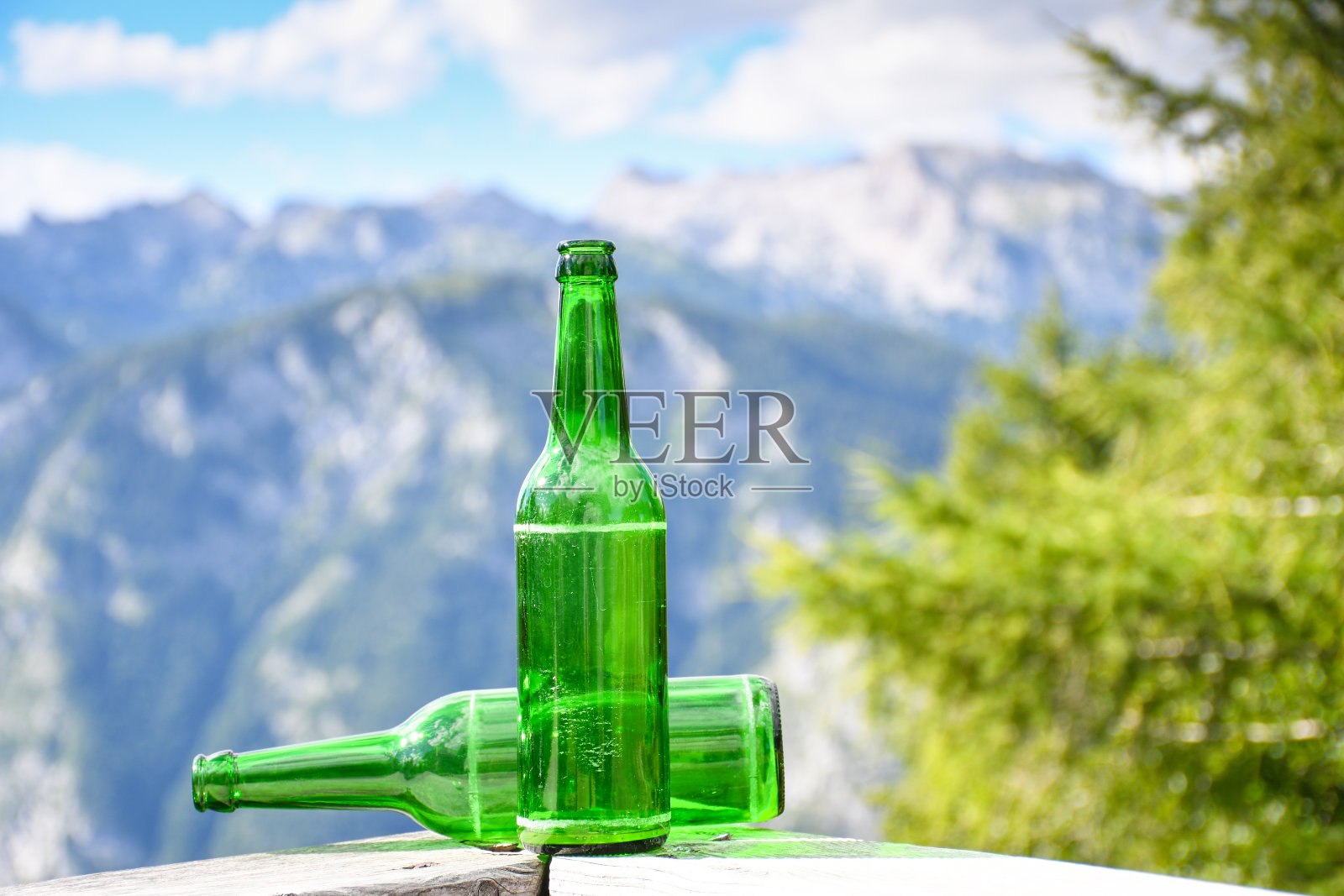 在高山上的木栅栏上放着绿色的空啤酒瓶照片摄影图片