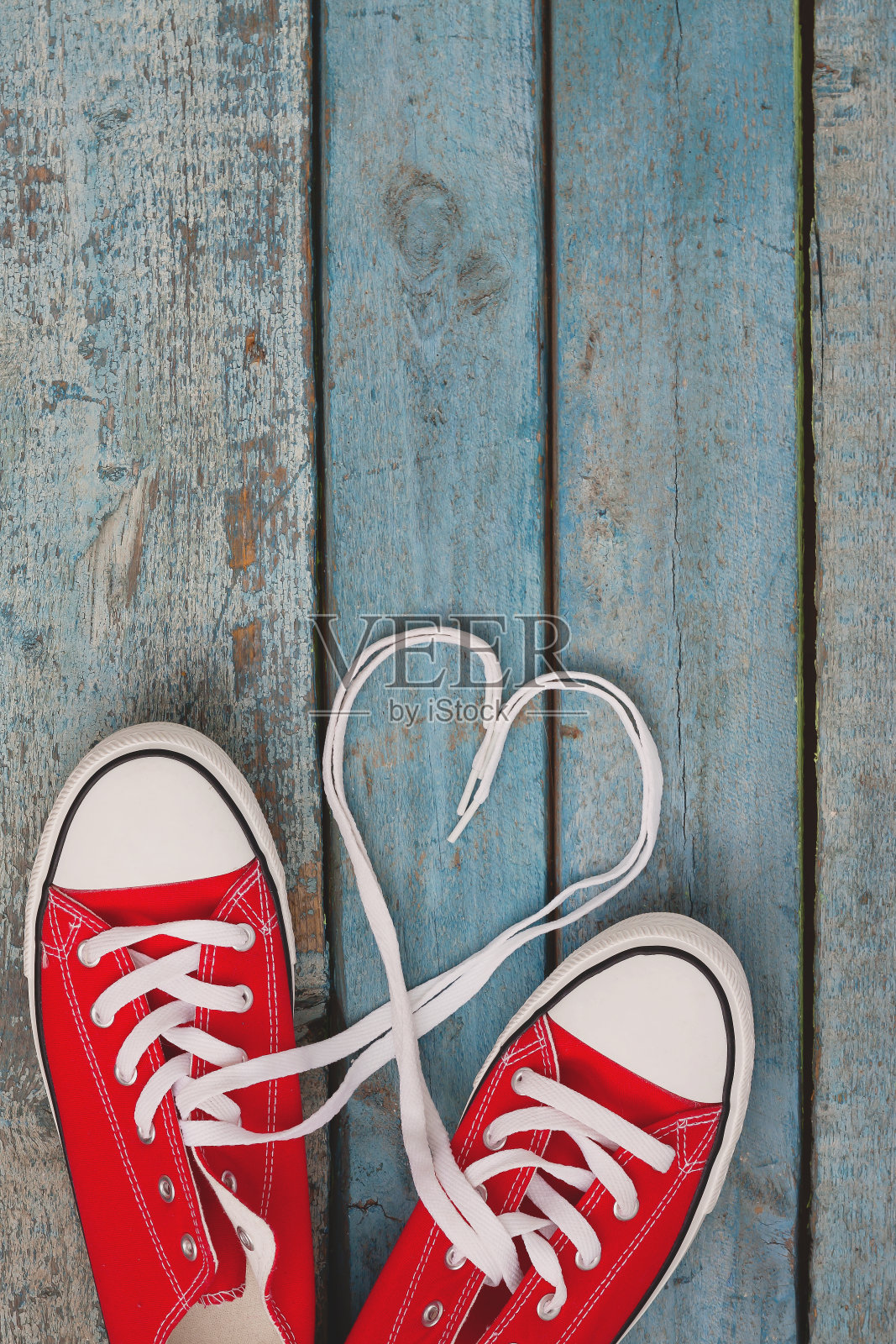 一双红色复古运动鞋上的蓝色木制背景，花边内衬在一个心的形状。年轻潮人爱的概念照片摄影图片