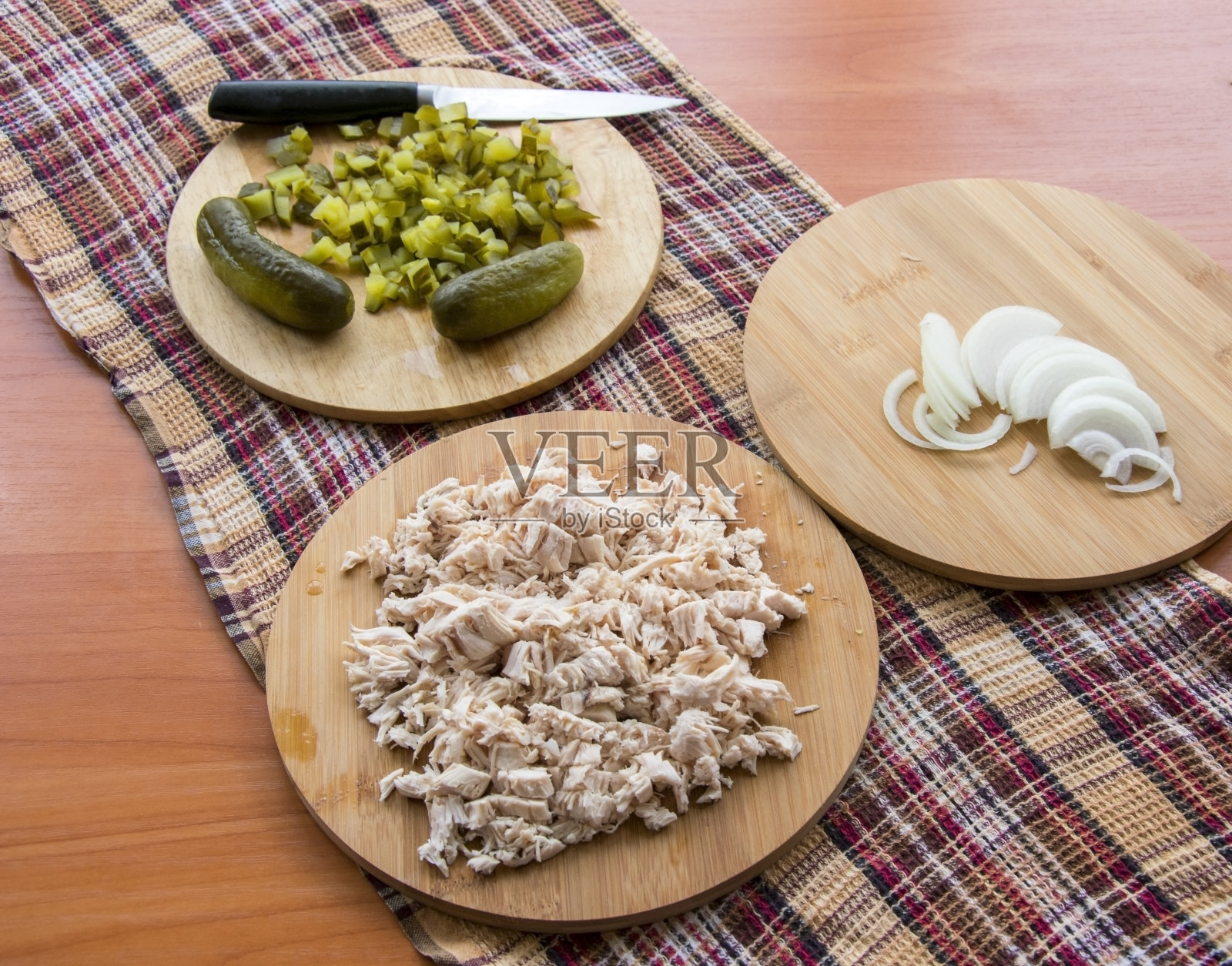 切碎的腌黄瓜放在砧板上，用刀切;木桌上放着煮熟的鸡肉和洋葱，上面放着格子厨房毛巾照片摄影图片