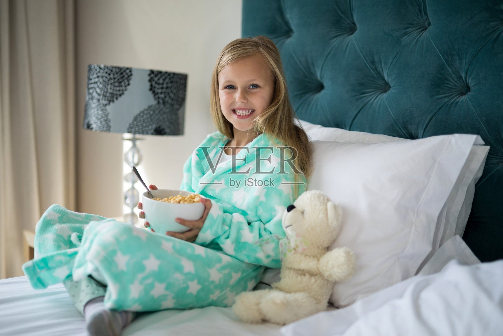 微笑的女孩在吃早餐，小熊在床上照片摄影图片