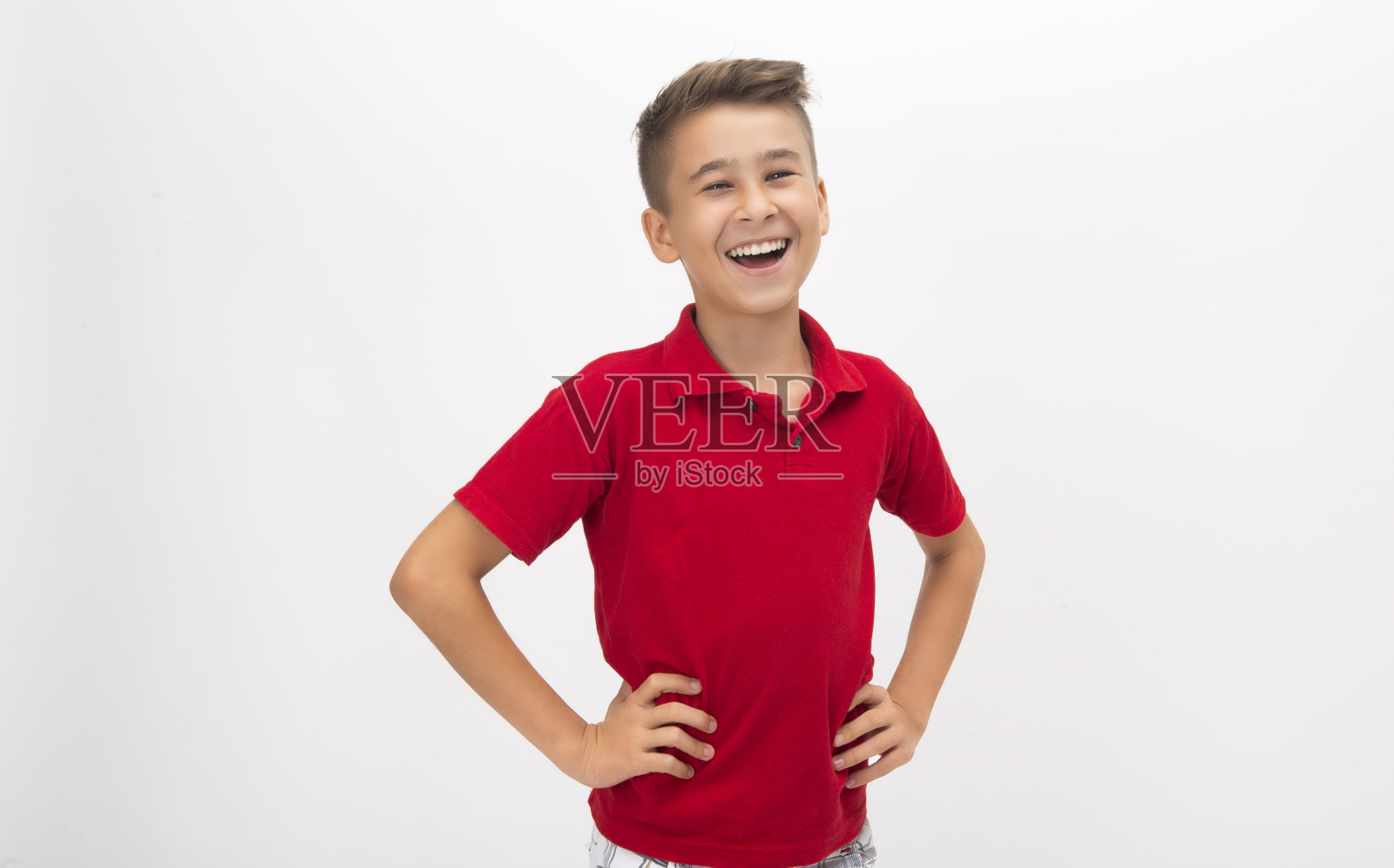 一个笑着的小男孩站在白色背景前，双手叉腰看着相机照片摄影图片