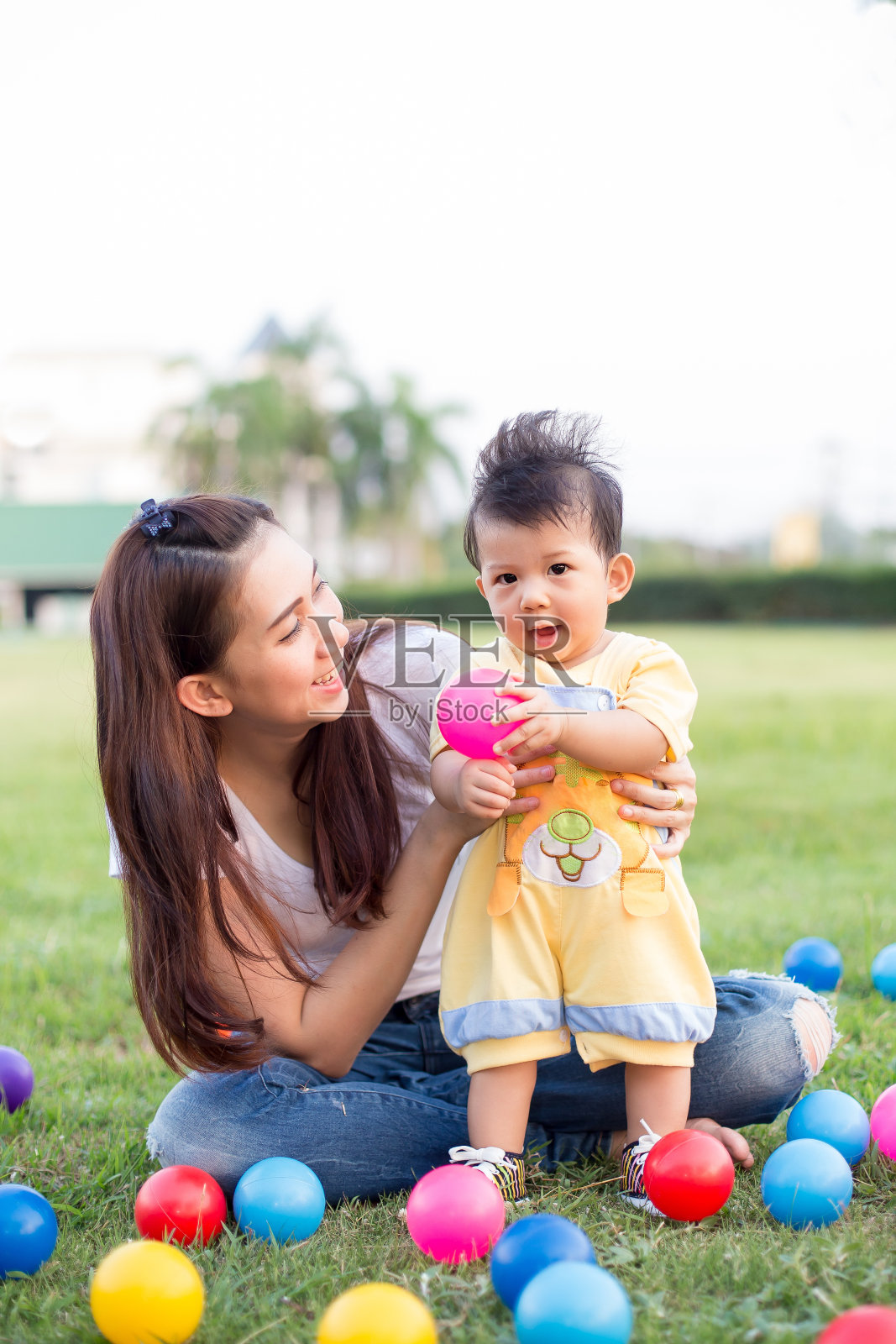 小男孩和妈妈在绿色的草地上玩彩色的球照片摄影图片