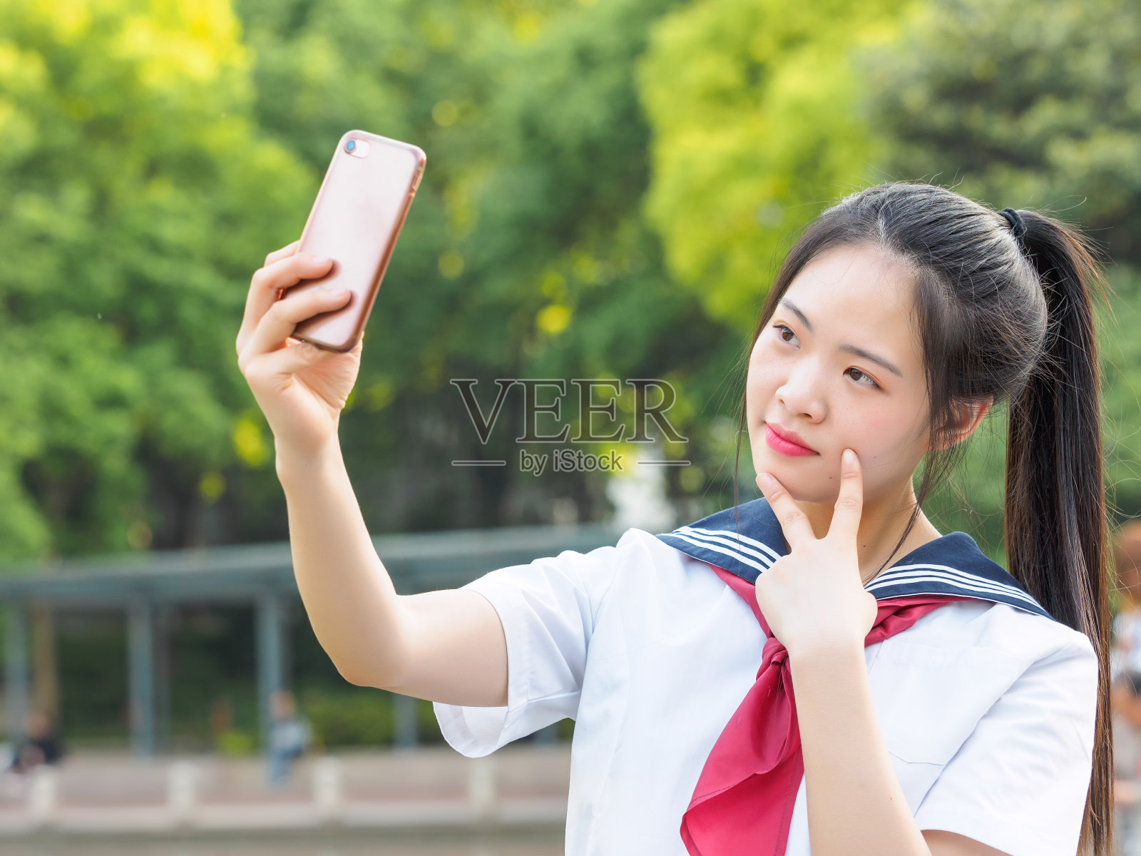 中国女学生穿着校服，用智能手机自拍。照片摄影图片