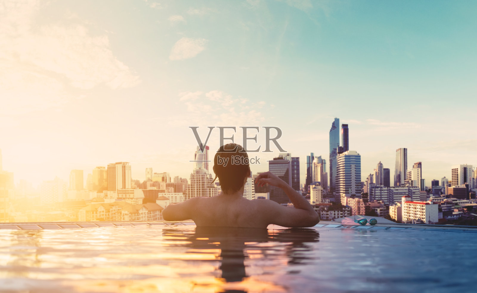 一个男人在日出的游泳池里放松，在城市的屋顶上照片摄影图片