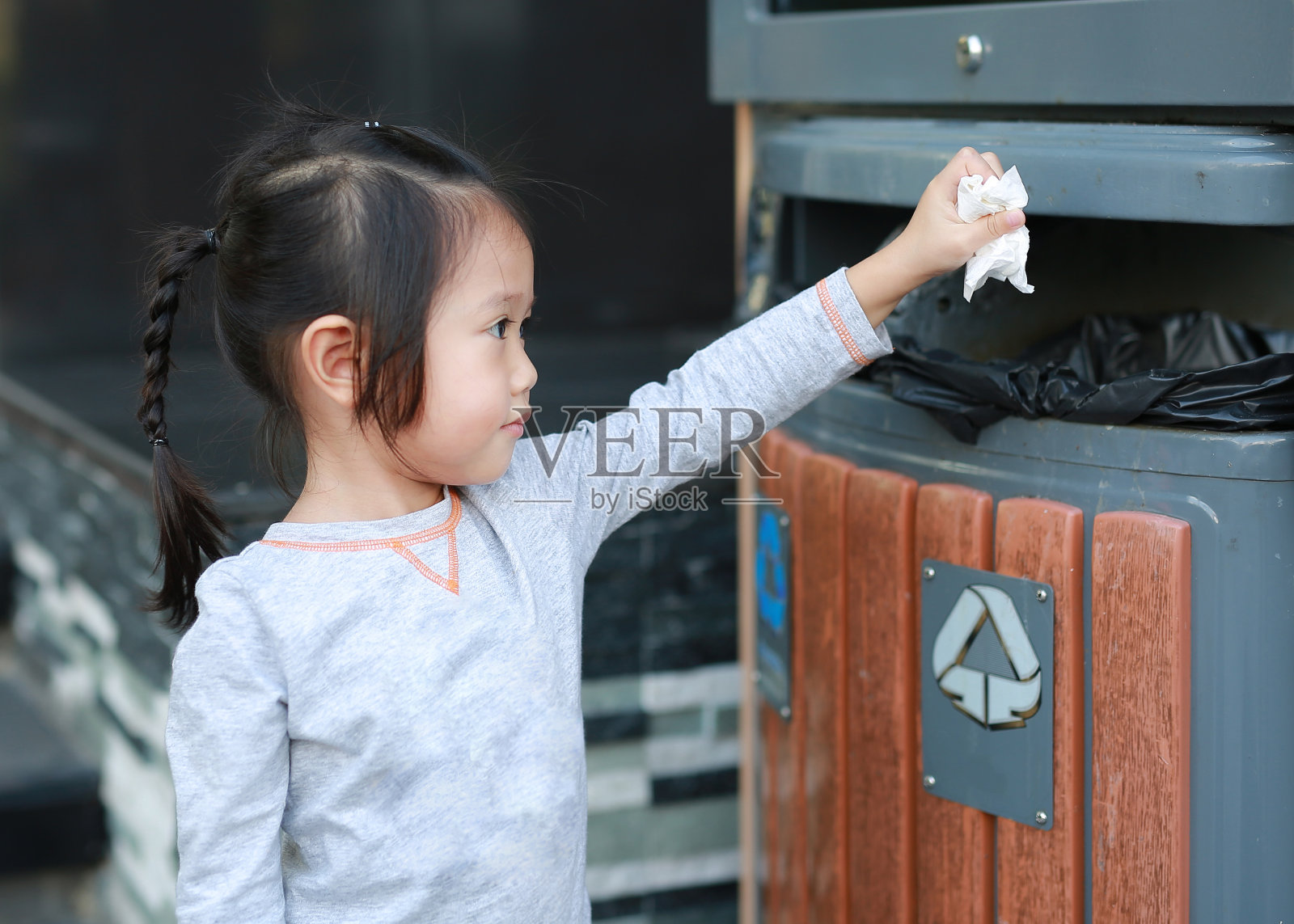 可爱的小女孩把垃圾放在户外的垃圾桶里。照片摄影图片