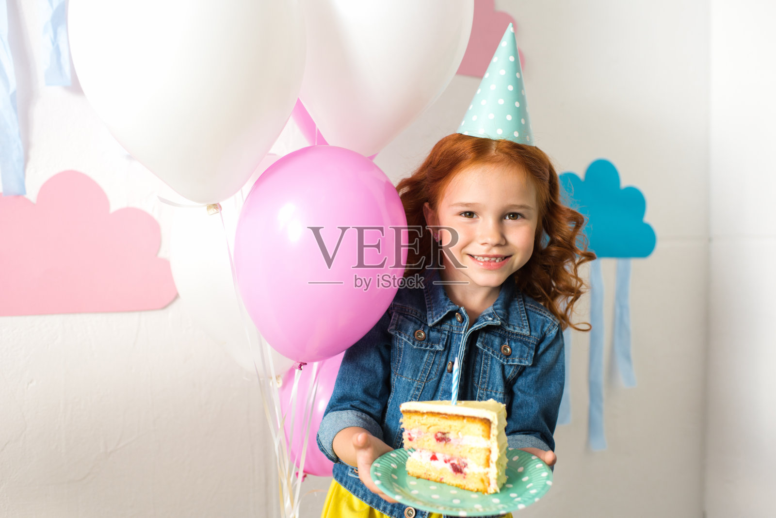 可爱的红发女孩戴着派对帽，拿着生日蛋糕，对着镜头微笑照片摄影图片