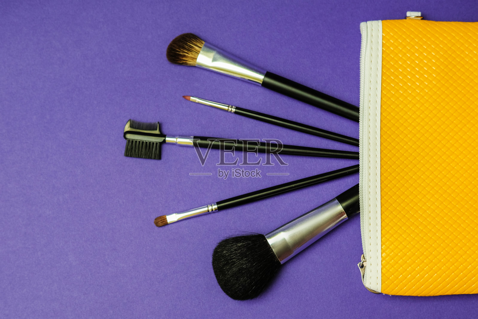 化妆刷在黄色化妆包在明亮的紫色背景。照片摄影图片