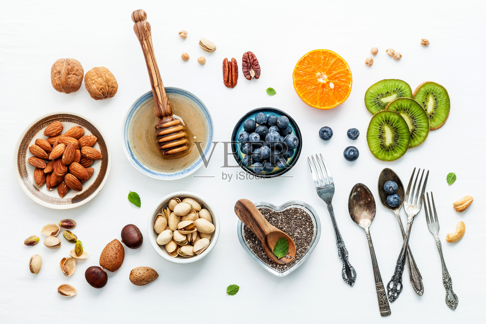 健康食品的配料背景，坚果，蜂蜜，浆果，水果，蓝莓，橘子，杏仁，核桃和奇异子。健康食品的概念建立在白色的木制背景上。平的。照片摄影图片