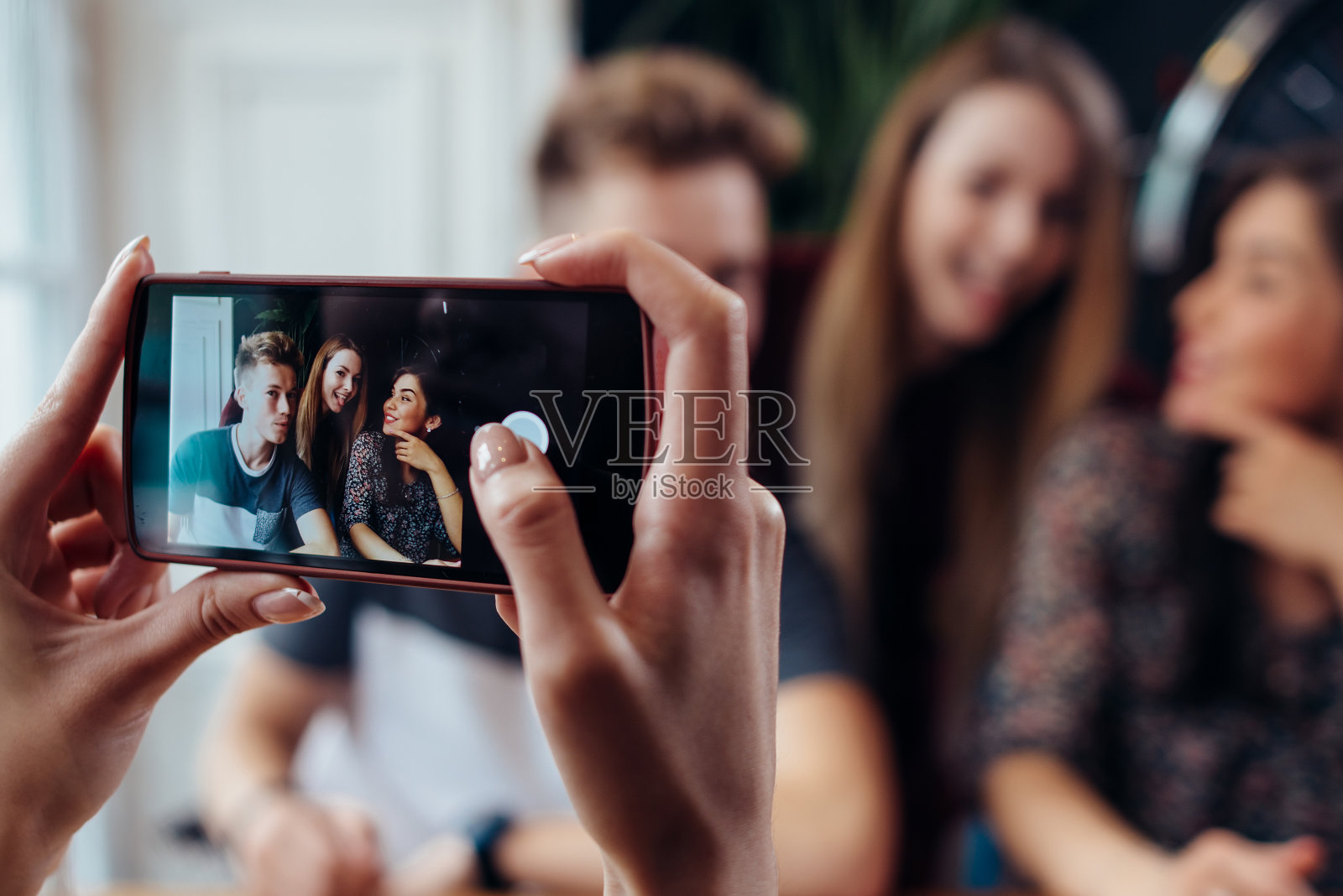 女性用智能手机拍下年轻开朗的朋友，模糊的背景照片摄影图片