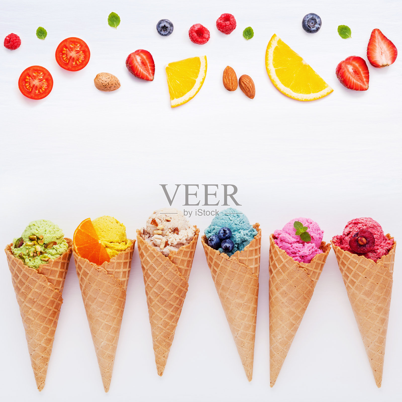 各种口味的冰淇淋圆锥蓝莓，草莓，开心果，杏仁，橙子和樱桃设置在白色的木制背景。夏季和甜蜜的菜单概念。照片摄影图片