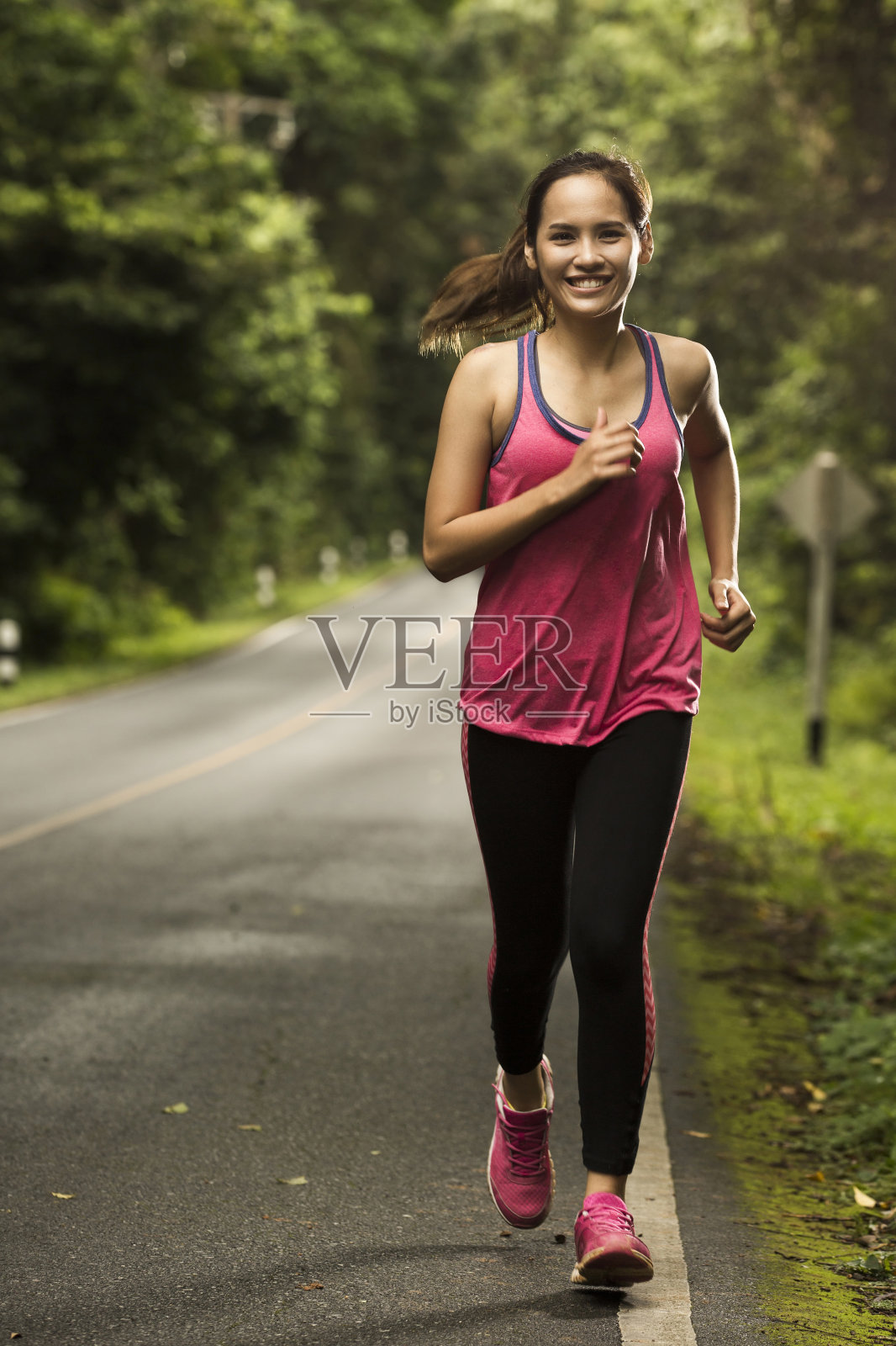 一个亚洲女人在阳光明媚的森林里的路上慢跑照片摄影图片