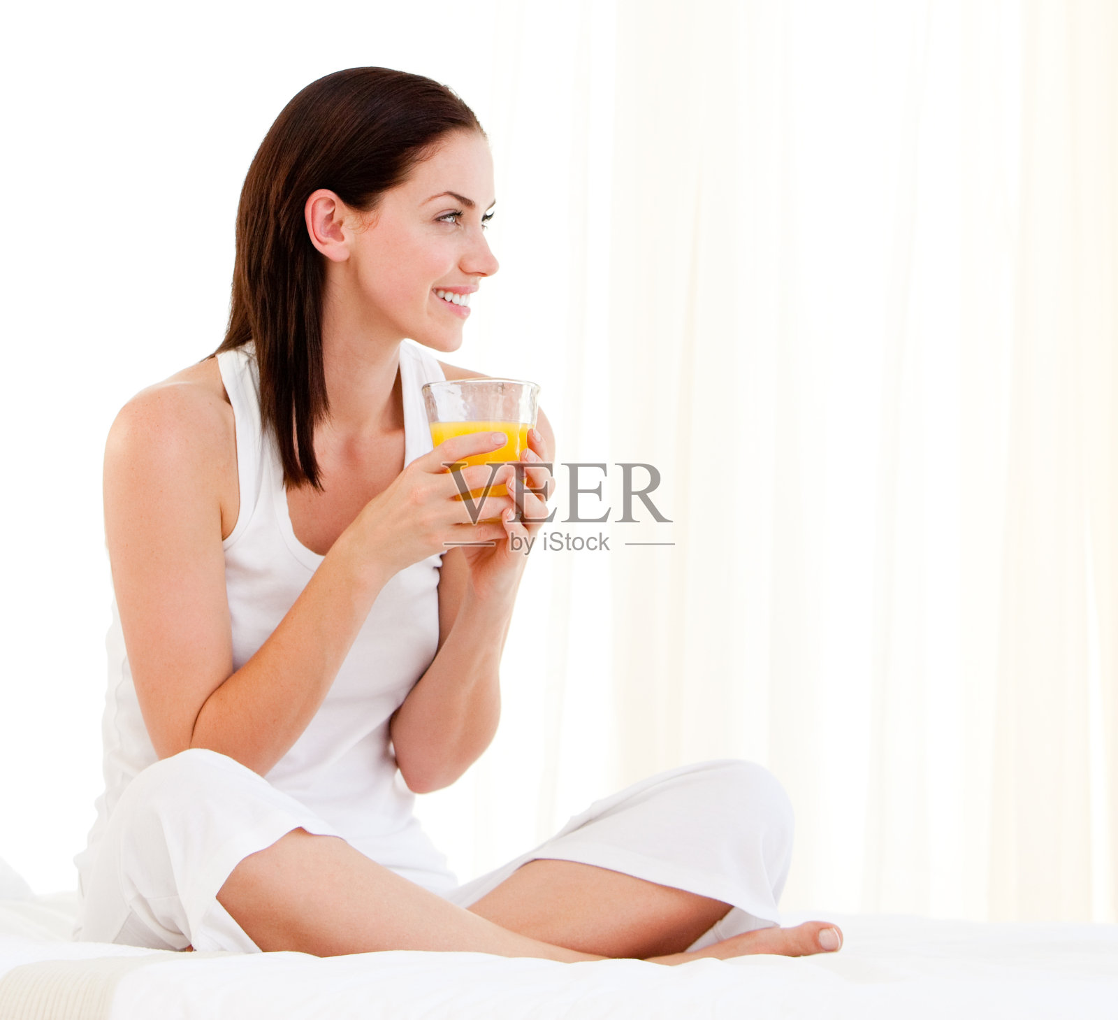 快乐的女人坐在床上喝着橙汁照片摄影图片