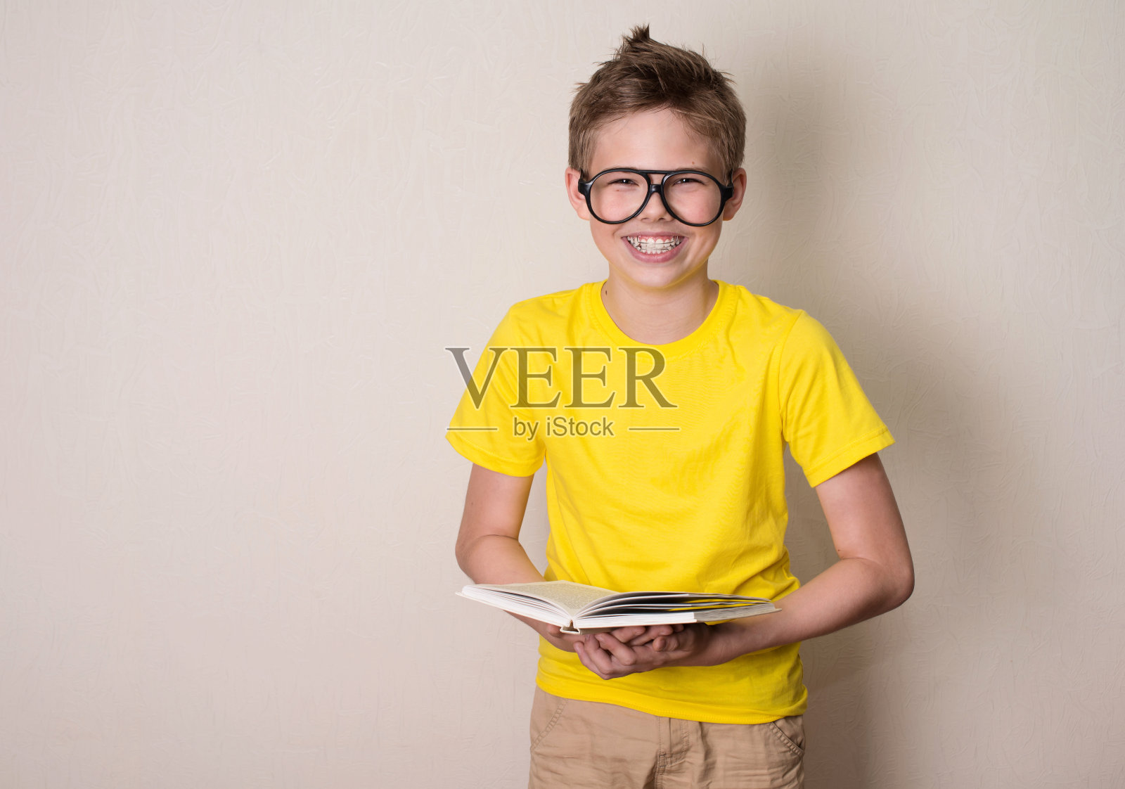 健康、教育和人的观念。快乐的少年在牙套和眼镜拿着一本书和笑。照片摄影图片