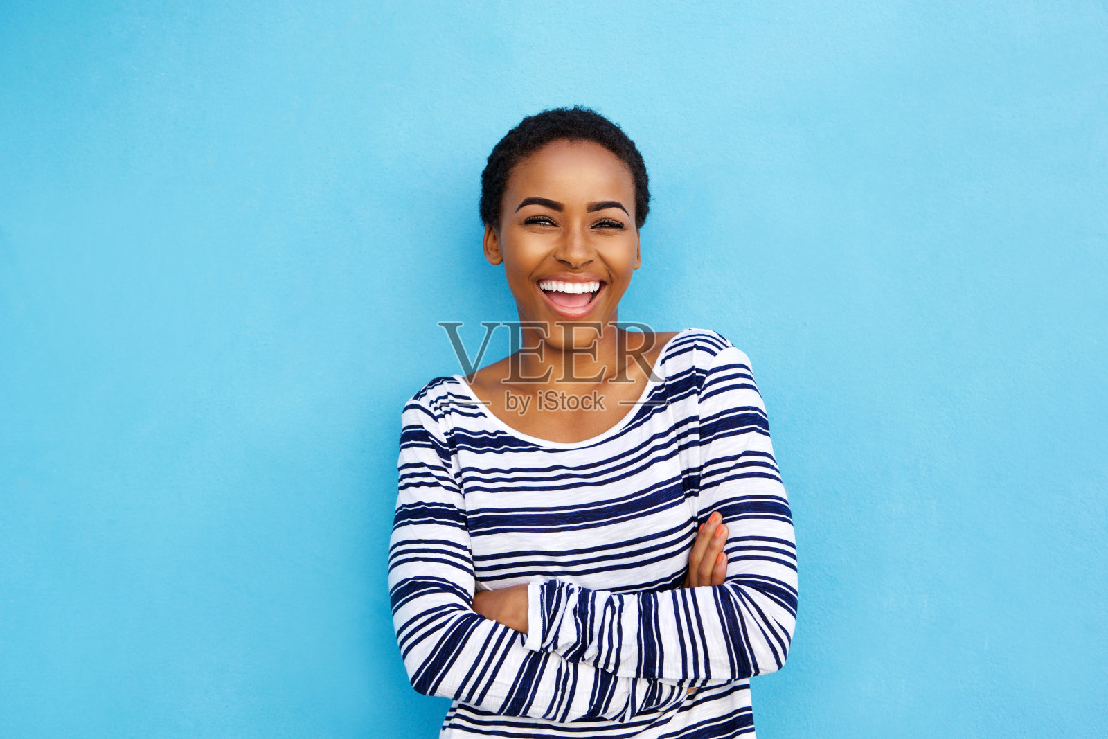 快乐的年轻黑人妇女对着蓝色的墙笑照片摄影图片