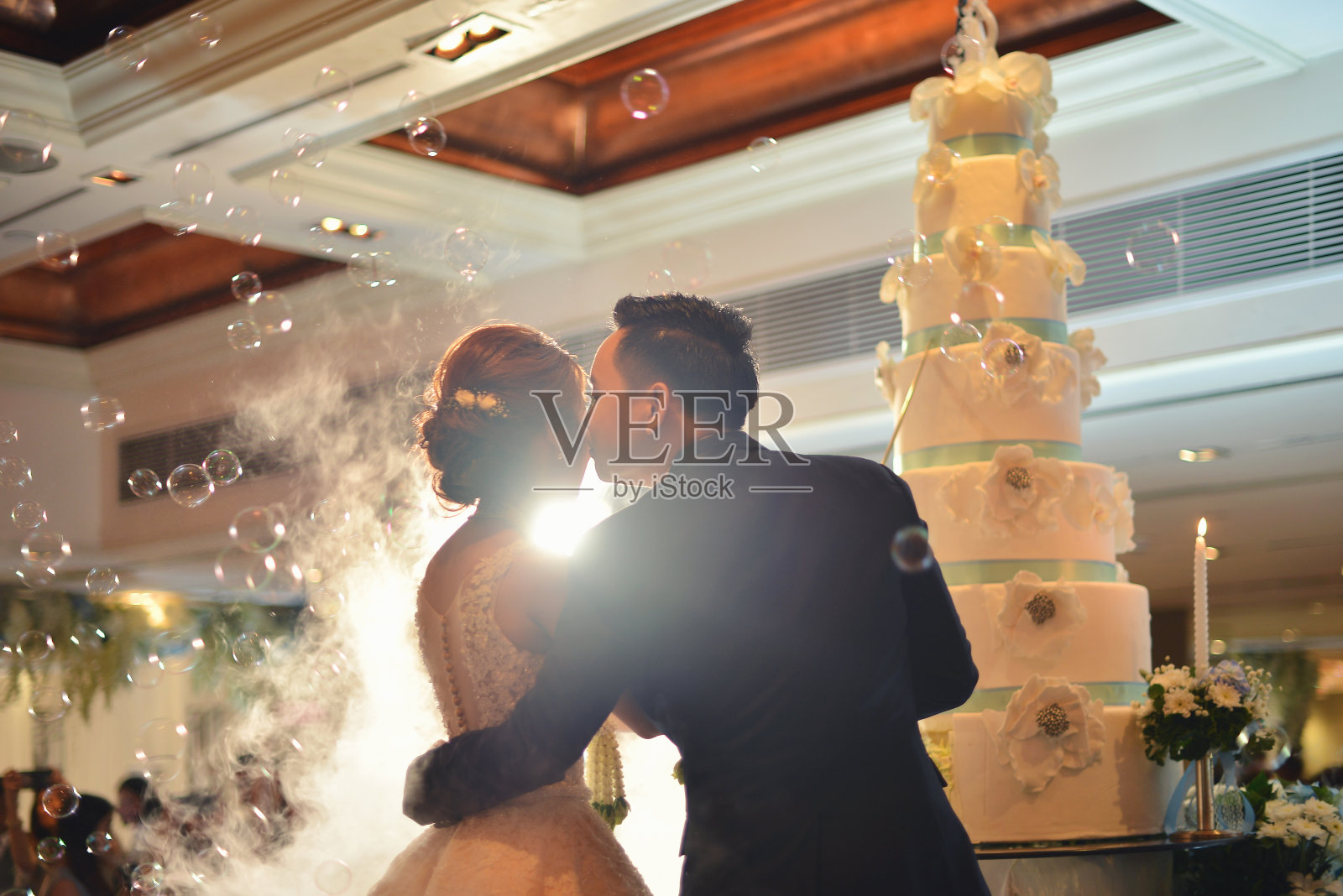 在礼堂举行的婚礼上，新郎在蛋糕前亲吻新娘照片摄影图片