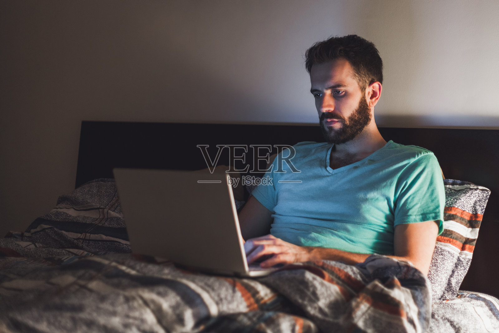 一个年轻人在床上用笔记本电脑工作到很晚照片摄影图片