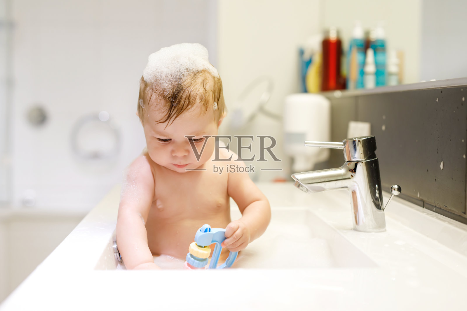 可爱可爱的宝宝在洗脸盆里洗澡，玩水和泡沫照片摄影图片