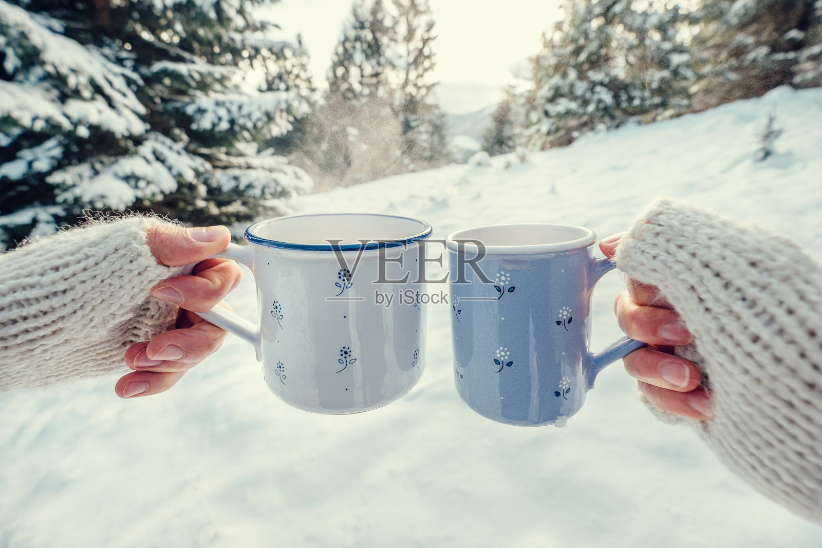 在冬天的森林里，两只手戴着连指手套拿着一个装有热茶的杯子照片摄影图片