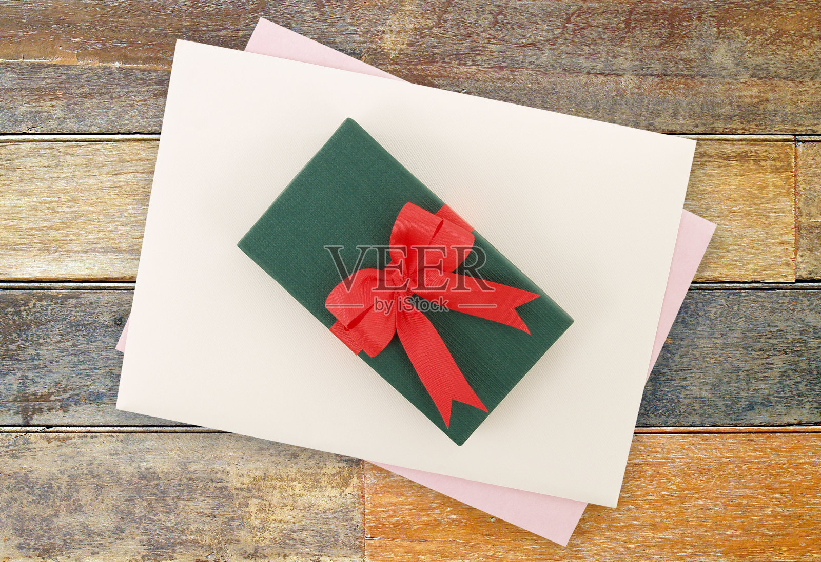 小的绿色礼品盒，红色蝴蝶结，白色信封和浅紫色的贺卡放在木地板上照片摄影图片